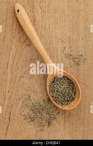 Feuilles de romarin séché en cuillère en bois sur fond de bois de teck . Banque D'Images