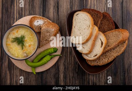 vue de dessus de la soupe d'orzo de poulet dans un bol et des poivrons sur la planche à découper avec des tranches de pain blanc de rafle et de seigle dans un bol sur fond de bois Banque D'Images