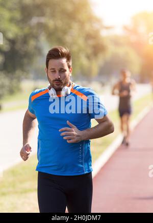 Un homme charmant et satisfait qui court sur la piste rouge.Jogging urbain le matin Banque D'Images