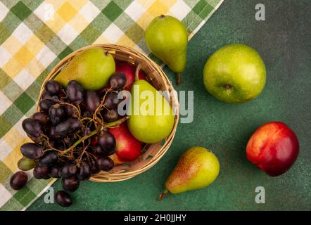 vue de dessus des fruits comme le raisin de pêche et la poire dans le panier sur tissu écossais avec pomme sur fond vert Banque D'Images