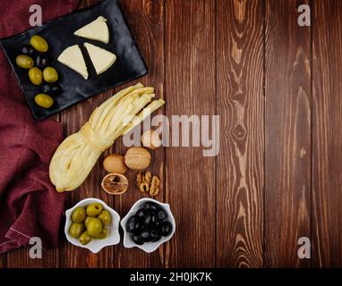 vue de dessus du fromage à la crème en forme de triangle avec des olives marinées sur un plateau noir et des noix avec du fromage à cordes sur fond de bois foncé avec un photocopieuse Banque D'Images