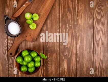 vue de dessus de prunes vertes en tranches avec sel et couteau de cuisine sur une planche à découper en bois et prunes dans un bol sur fond de bois rustique avec espace de copie Banque D'Images