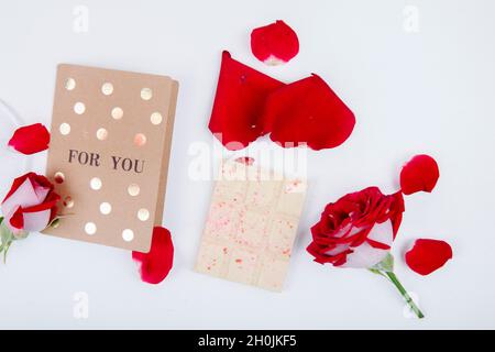 vue du dessus de la rose rouge avec petite carte postale et chocolat blanc avec pétales de rose rouge sur fond blanc Banque D'Images