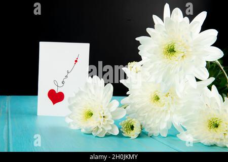vue latérale sur les fleurs de chrysanthème blanc et une carte postale sur fond de bois bleu Banque D'Images
