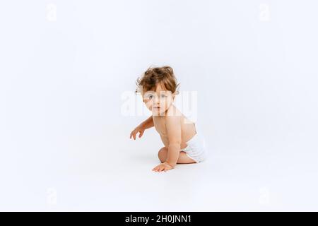 Portrait d'un petit garçon mignon, bébé dans un couches curieusement en regardant loin isolé sur fond blanc de studio Banque D'Images