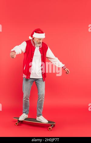 pleine longueur de l'homme d'âge moyen dans le chapeau de santa à cheval skateboard sur le rouge Banque D'Images