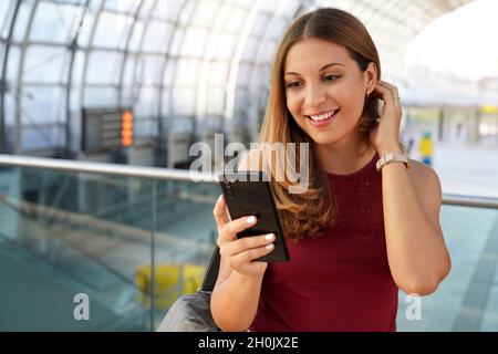 Voyages et technologie.Une jeune femme excitée qui reçoit de bonnes nouvelles sur son smartphone attend d'embarquer dans le terminal de l'aéroport. Banque D'Images