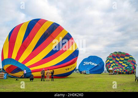 Trois ballons à air chaud au sol sont préparés pour le vol avec un groupe de personnes debout à regarder. Banque D'Images