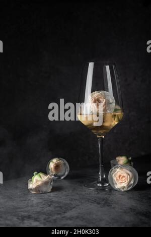 un verre de vin ambré avec des boutons de roses blanches de brousse dans la glace. sur un fond sombre, copyspace.Touche Bas Banque D'Images