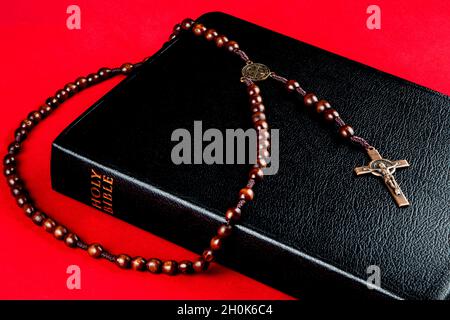 Perles de rosaire en bois et crucifix avec bible sur fond rouge Banque D'Images