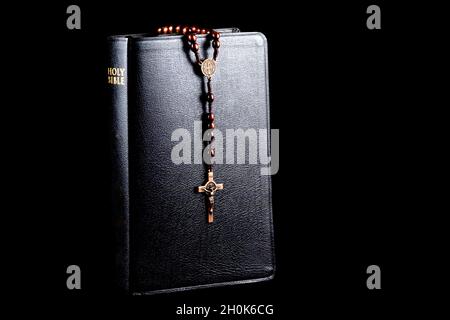 Bible avec des perles de rosaire en bois et crucifix isolé sur fond noir Banque D'Images
