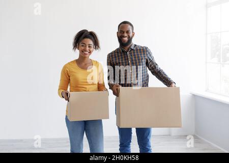 Souriante femme et homme afro-américain millénaire portent des boîtes en carton avec des objets dans la chambre vide Banque D'Images