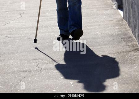 Homme marchant avec une canne en bas de la rue, ombre sur l'asphalte.Notion de vieillesse, maladies de la colonne vertébrale ou maladie articulaire, personnes âgées Banque D'Images