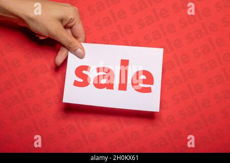 main féminine tient un morceau de papier avec l'inscription vente sur fond rouge fort carton avec la vente écrite sur pour promouvoir des ventes spéciales Banque D'Images