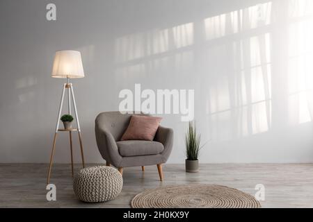 Fauteuil avec coussin, lampe, plante dans la marmite, pouf et tapis rond sur fond de mur gris dans la salle de séjour Banque D'Images