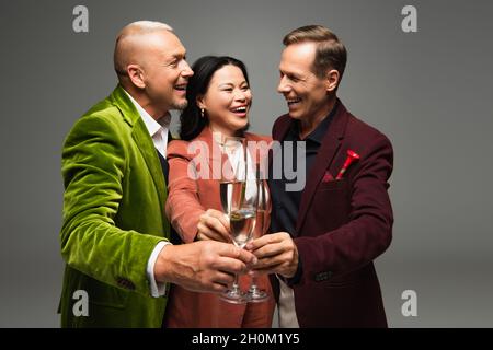 Des amis interraciaux heureux toaster le champagne pendant la fête isolée sur gris Banque D'Images