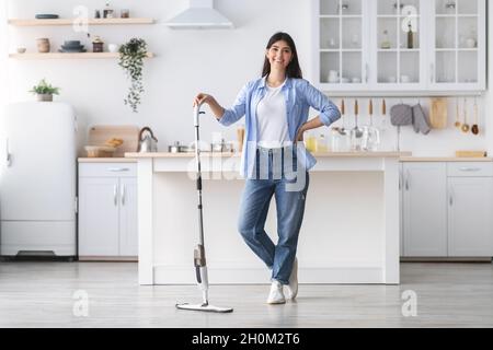 Portrait d'une femme gaie qui nettoie le sol avec une vadrouille vaporisée, pose Banque D'Images