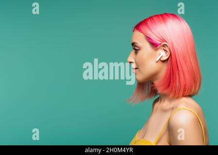 vue latérale d'une jeune femme aux cheveux teints de rose dans un écouteur sans fil isolé en bleu Banque D'Images