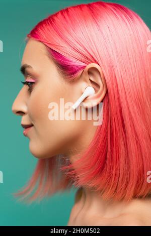 profil de la jeune femme aux cheveux teints roses dans les écouteurs sans fil isolés sur le bleu Banque D'Images