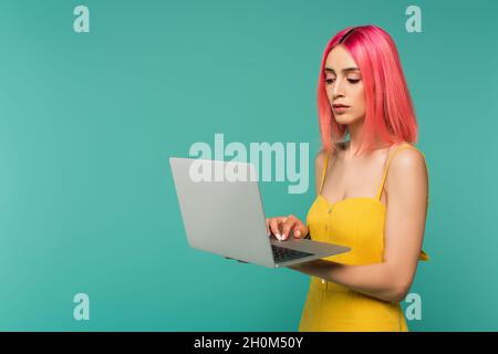 jeune femme aux cheveux teints roses utilisant un ordinateur portable isolé sur bleu Banque D'Images