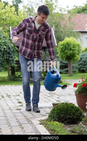 Beau homme arroser des fleurs dans le jardin.Concept de soins infirmiers en usine Banque D'Images