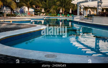 Piscine moderne et luxueuse avec parasols et chaises longues entourés de palmiers exotiques Banque D'Images