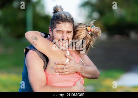 Un homme sportif sourit tout en embrassant une femme dans un parc Banque D'Images