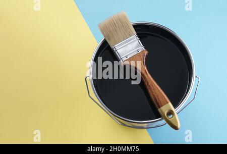 Pinceau en bois sur peinture noire peut sur fond bleu et jaune Banque D'Images