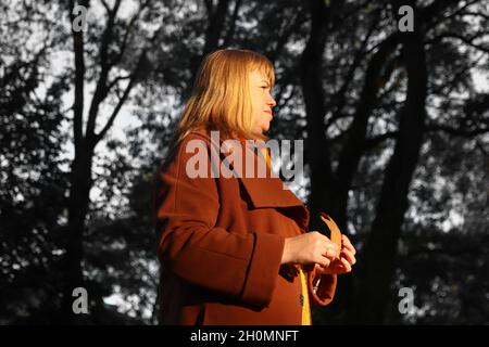 Portrait d'une femme blonde de race blanche d'âge moyen dans le parc d'automne.Femme lumineuse et élégante en manteau orange et châle de cou marchant dans le parc d'octobre.Triste automne Banque D'Images