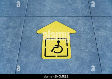 Dessin d'un fauteuil roulant sur une flèche jaune collée au carrelage de la salle d'attente.Signe de direction du mouvement Banque D'Images