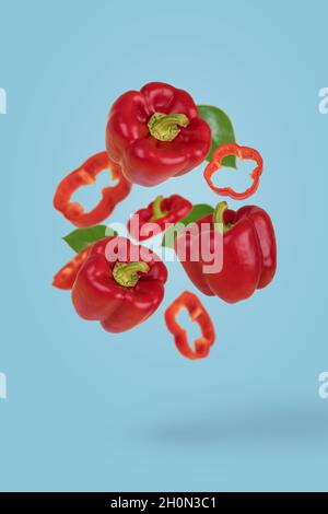 Idée créative avec des poivrons rouges entiers et coupés en tranches, frais et mûrs, volant dans l'air, isolés sur fond bleu.Alimentation saine, alimentation, vitamines, alimentation à la mode p Banque D'Images