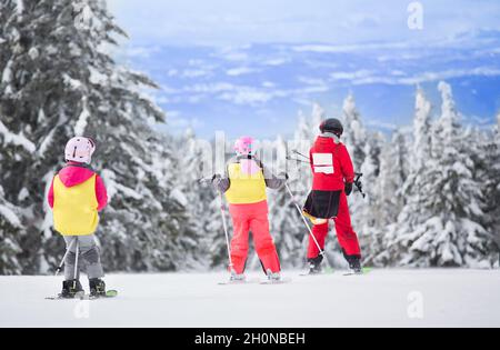 Groupe d'enfants apprenant à skier sur la pente avec un instructeur.Ciel bleu et firs blancs en arrière-plan Banque D'Images