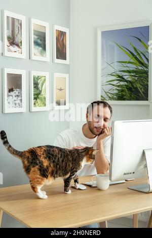 Travailler à domicile sur le verrouillage de l'épidémie de coronavirus : homme millénaire indépendant avec chat dans un bureau distant Banque D'Images