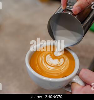 Main du barista préparant du Latte ou du cappuccino verse du lait prépare du Latte Art. Carré photo. Banque D'Images