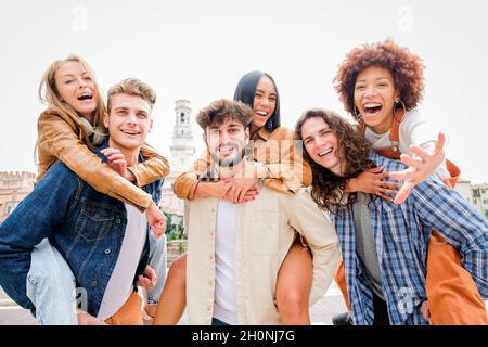 Jeunes amis ayant du plaisir à l'extérieur - six étudiants à l'extérieur, des hommes portant deux filles sur leur dos Banque D'Images