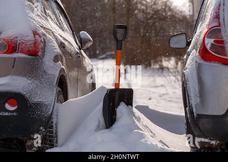 petite pelle en plastique qui dépasse d'une dérive de neige entre deux voitures en stationnement après une tempête de neige Banque D'Images