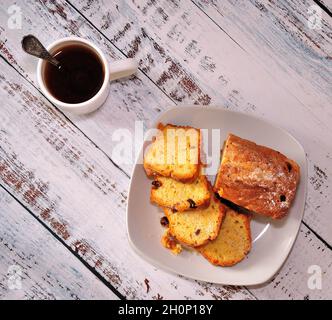 Assiette blanche avec des muffins frais en tranches et une tasse de thé noir sur une table en bois.Pose à plat. Banque D'Images