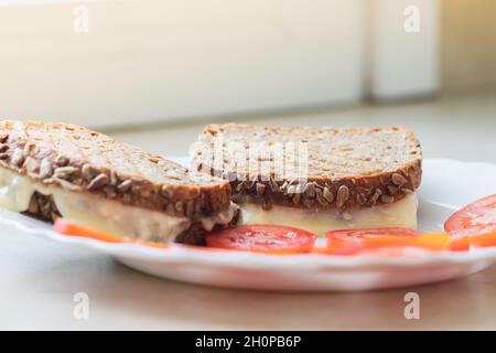 Griller des tranches de pain à base de farine orthographiée, fourrées de fromage, à côté de tomates tranchées, sur une assiette en porcelaine blanche. Arrière-plan flou Banque D'Images