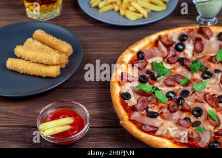 Pizza sur un plateau gros plan sur la table avec ketchup, jus, sauce et pommes de terre sur une table en bois sombre dans le style rustique. Banque D'Images