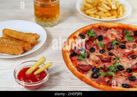 Restauration rapide.Pizza sur un plateau gros plan sur une table en bois blanc avec ketchup, jus, sauce et pommes de terre. Banque D'Images