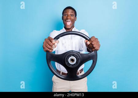 Photo de la peau douce et foncée impressionnée homme porter chemise blanche souriant tenant le volant isolé couleur bleu arrière-plan Banque D'Images