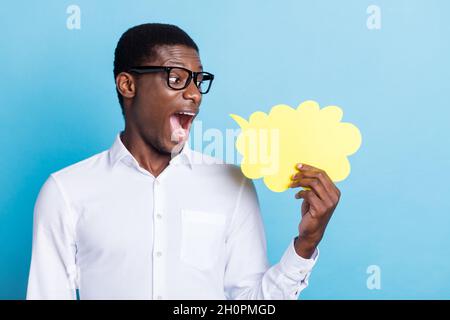 Photo de la peau sombre impressionnée homme porter blanc chemise lunettes tenant esprit nuage vide espace isolé bleu couleur arrière-plan Banque D'Images