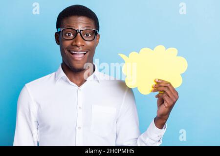 Photo de drôle excitée peau sombre gars habillé chemise verres tenant parler bulle vide espace isolé couleur bleu fond Banque D'Images