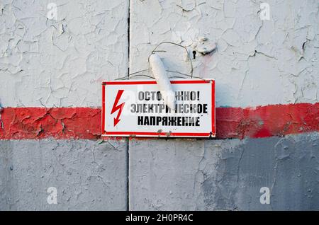 Attention.Haute tension.Panneau d'avertissement rouge sur une porte en métal.En russe Banque D'Images