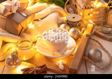 Ambiance de Noël avec une tasse de café avec des guimauves et des décorations de Noël dans l'éclairage de soirée avec guirlande lumineuse. Banque D'Images