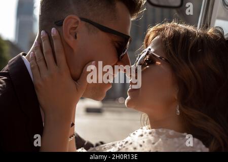 baiser tendre de la mariée et du marié dans des lunettes de soleil sur le fond du paysage urbain en contour lumière pressé nez l'un à l'autre heureux ensemble, Banque D'Images