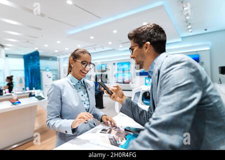 Jeune couple multiculturel à la recherche d'un nouveau smartphone à acheter.Femme regardant le catalogue tout en tenant un smartphone. Banque D'Images