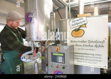 11 octobre 2021, Saxe, Fuchshain BEI Leipzig: Le jardinet paysagiste de Leipzig Andreas Richter (r), qui a installé son broyeur mobile de pommes pour une journée dans une ferme de Fuchshain, vérifie le jus de pomme fraîchement pressé des fruits apportés par ses clients.Devant les yeux de ses clients, la petite usine de fruits sur roues va transformer les fruits riches en vitamines en jus direct naturellement nuageux à divers endroits jusqu'à la fin du mois d'octobre et peut ensuite être emmenée à la maison en paquets de 5 litres.Avec la cidery mobile, Andreas Richter veut contribuer à la préservation, mais aussi à la Banque D'Images