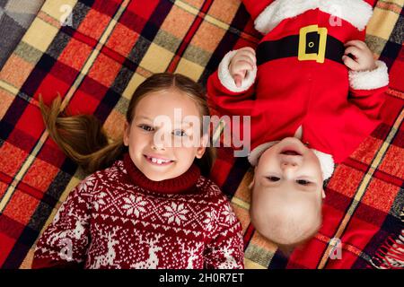 Photo de doux mignon petit frère soeur vêtue pull-over imprimé sourire couché à carreaux couverture à carreaux à l'intérieur maison maison chambre Banque D'Images