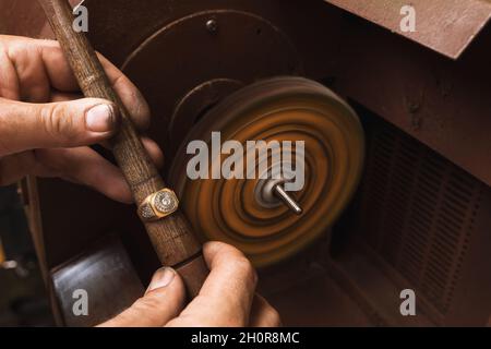 Un bijoutier polit une bague dorée sur une machine spéciale dans un atelier Banque D'Images